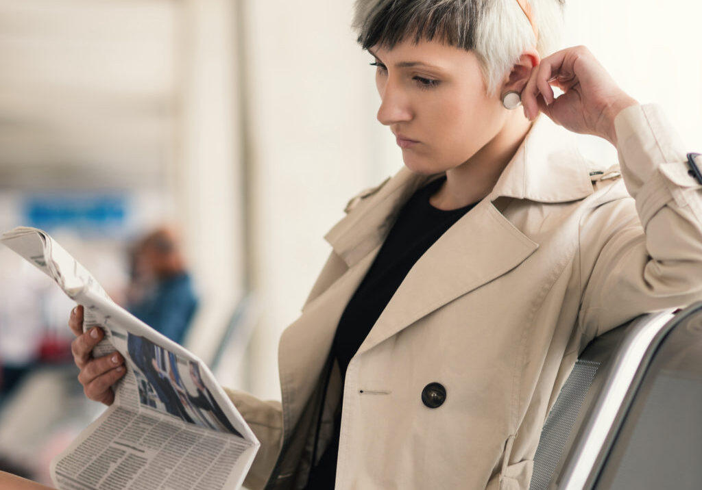 Businesswoman reading newspaper at Charles de Gaulle airport, Paris.