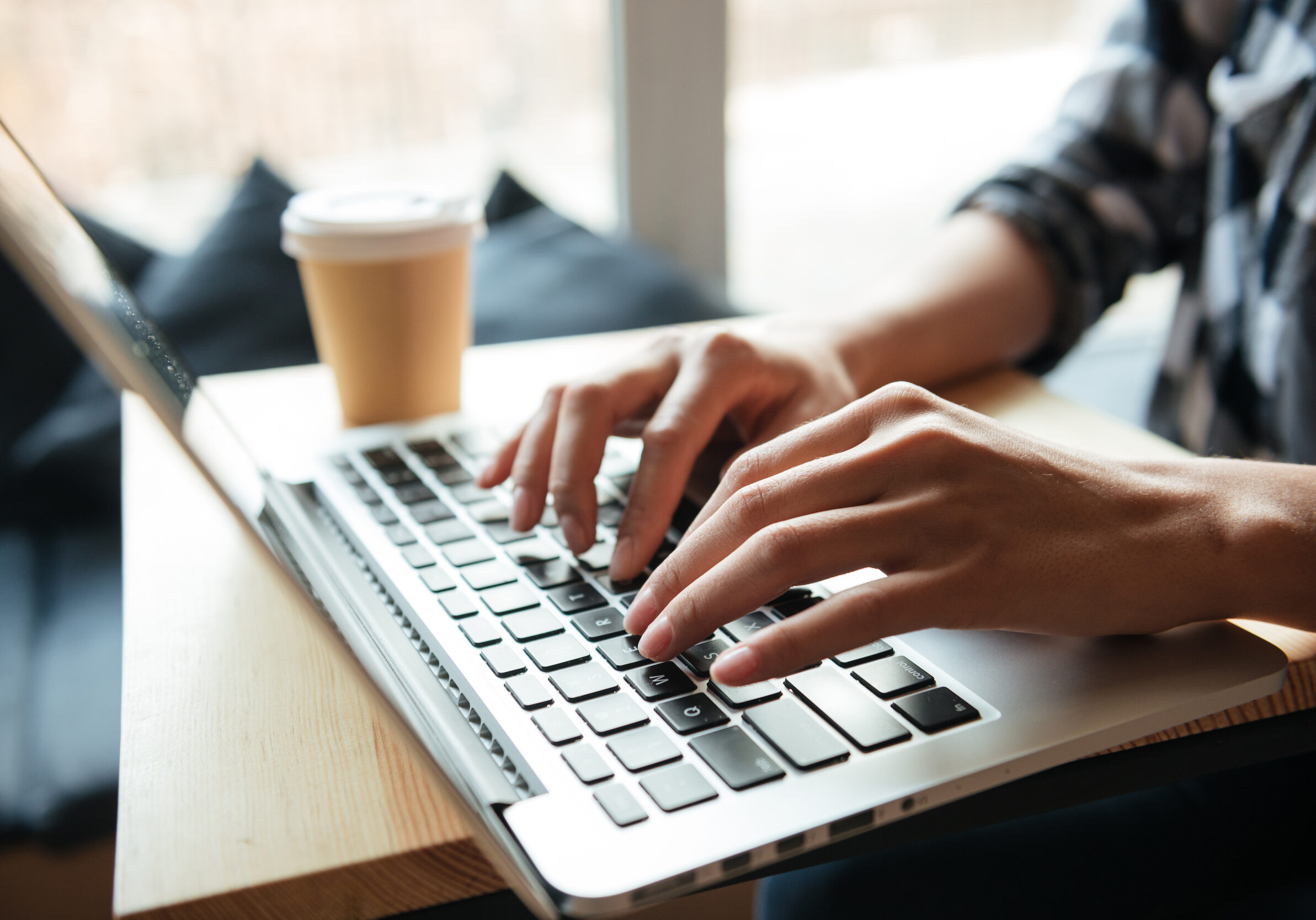 Cropped image of amazing young caucasian lady sitting indoors using laptop computer and drinking coffee. Coworking concept.